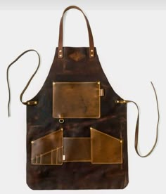 a brown leather apron with brass hardwares and straps on the front, hanging from a white wall