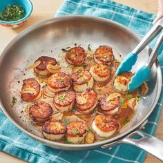 a pan filled with cooked scallops on top of a wooden table next to a blue towel