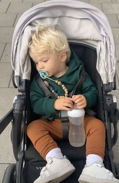 a young boy sitting in a stroller with a pacifier in his mouth and wearing a green hoodie