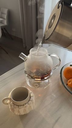 tea being poured into a glass pitcher on a table with oranges and crochet