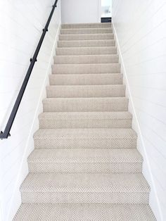 a white staircase with beige carpet and black handrails