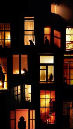 people are standing in the windows of a house at night with their hands up and lights on