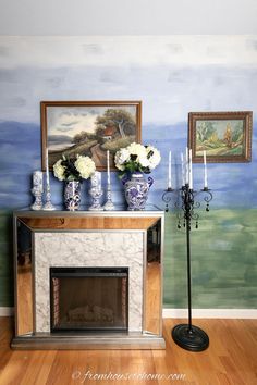 a fireplace with vases and flowers on it in front of a painted wall behind it