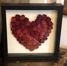 a heart made out of rolled up roses in a shadow box frame on a table