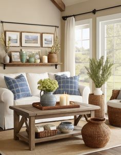 a living room with white couches and blue pillows on the coffee table in front of a window