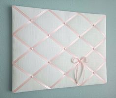 a white wall with pink ribbon on it and a knot hanging from the middle of the frame