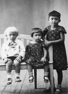 three children sitting on a bench in an old photo