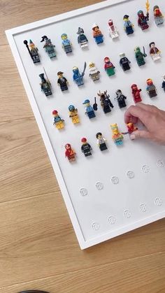 lego minifigures are displayed on a white board with black glasses and a person's hand pointing at them