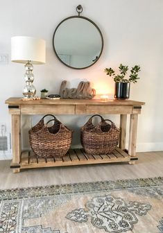 a wooden table with baskets on it in front of a mirror and lamp next to a rug