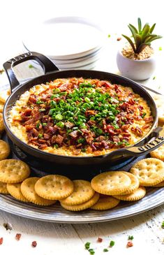 a platter filled with crackers and a large pot of dip on the side