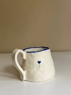 a white ceramic pitcher with blue handles on a table