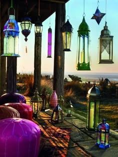 colorful lanterns hanging from the ceiling in front of an ocean and sand area at sunset