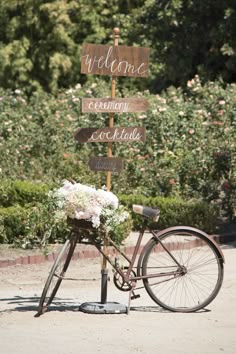 a bicycle parked next to a wooden sign with flowers on the front and welcome signs on the back