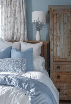 a bedroom with blue walls, white bedding and wooden dresser in the corner next to it