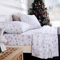 a christmas tree is in the corner of a room with white bedding and snowflakes