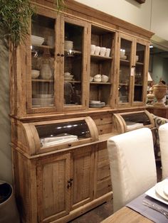 a wooden hutch with glass doors on the front and side, sitting next to a dining room table