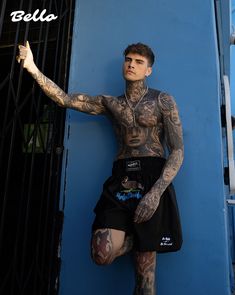 a tattooed man leaning against a blue wall