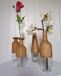 three wooden vases with flowers in them sitting on a white tableclothed surface