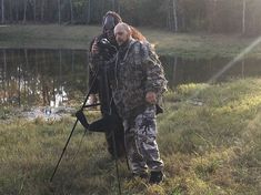 a man standing next to a camera on top of a field near a body of water