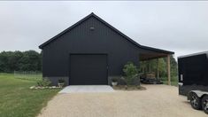 a black trailer parked in front of a barn with an open garage door on the side