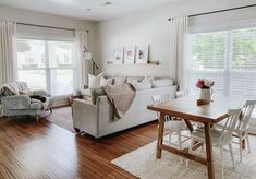 a living room filled with furniture and a wooden table in front of two large windows