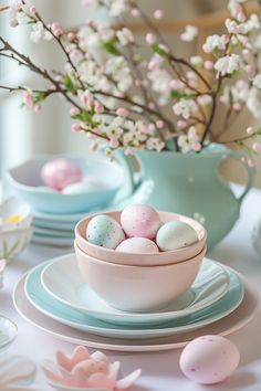 an easter table setting with pastel colored eggs in a blue bowl and pink flowers