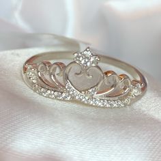 a wedding ring with a heart and crown design on the side, sitting on a white cloth