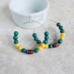 Score big with these custom wood beaded earrings in your team's colors, complete with football beads. Ideal for football moms supporting their little MVP! Beaded Hoop Earrings 🧡 Custom made in your football team's color(s) for a personalized touch 🤍 High-quality wood beads for durability and style, in 14 color options 💚 Hoops are 2.5" in diameter, and the overall length is 3.3" 💙 Lightweight and comfortable for all-day wear 💛 Free Shipping! MAKE THEM YOUR OWN Use the drop downs to select yo Diy Sports Earrings, Football Moms, Football Jewelry, Football Diy, Football Earrings, Mom Support, Sports Jewelry, Mom Jewelry, Football Mom