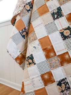 an orange and white patchwork quilt hanging on a wall next to a wooden floor