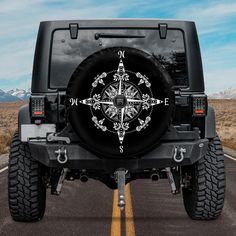 a black jeep with white compass on it's tire cover in the middle of an empty road