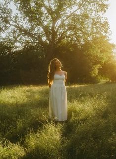 a woman in a white dress is standing in the grass with her hair blowing back