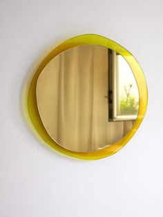 a yellow circular mirror hanging on the side of a white wall next to a window