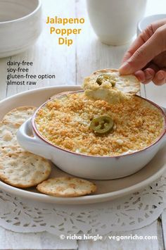 someone dipping jalapeno popper dip in a bowl with crackers on the side