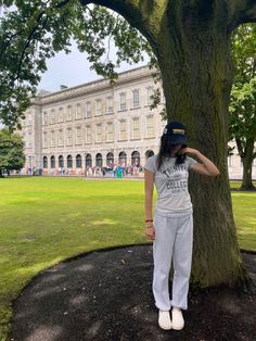 a woman standing next to a tree in front of a large building