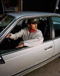 a man sitting in the driver's seat of a car wearing a baseball cap