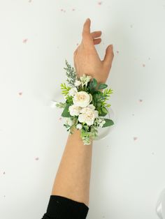 a woman's hand with a wrist corsage holding flowers and greenery