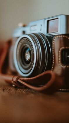 a camera sitting on top of a wooden table next to a brown leather case and strap