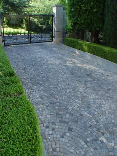 a brick driveway with an iron gate and black gate in the background, surrounded by green bushes