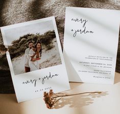 two wedding cards with the same photo on them are laying next to each other and one is holding a dried flower