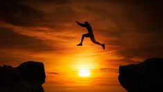 a person jumping off rocks into the ocean at sunset