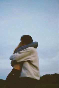 two people embracing each other in front of a blue sky