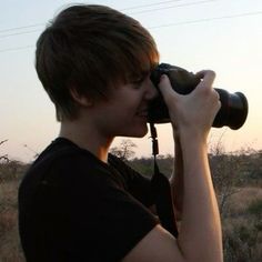 a person holding a camera up to their face with the sun setting in the background