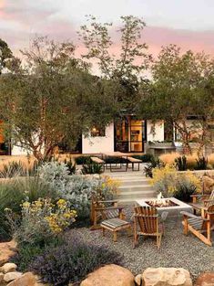 an outdoor dining area with chairs and tables surrounded by rocks, shrubs and trees in the background