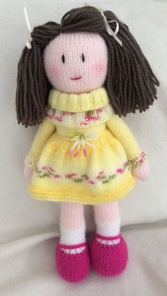 a knitted doll with brown hair wearing a yellow dress and pink shoes on a white sheet