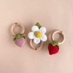 three crocheted strawberries and two wooden rings on a pink background with a flower