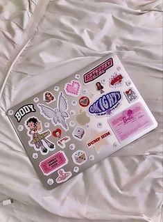 a laptop computer sitting on top of a bed covered in white sheets and stickers