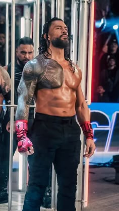 a man with long hair and tattoos standing in front of a metal cage holding a pink glove