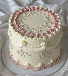 a three tiered cake with pink and white frosting on a plate, sitting on a bed sheet