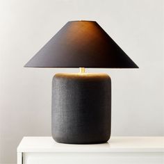 a black table lamp on top of a white dresser next to a gray and gold lamp shade