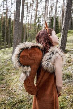 a woman in a brown dress is walking through the woods with her back to the camera